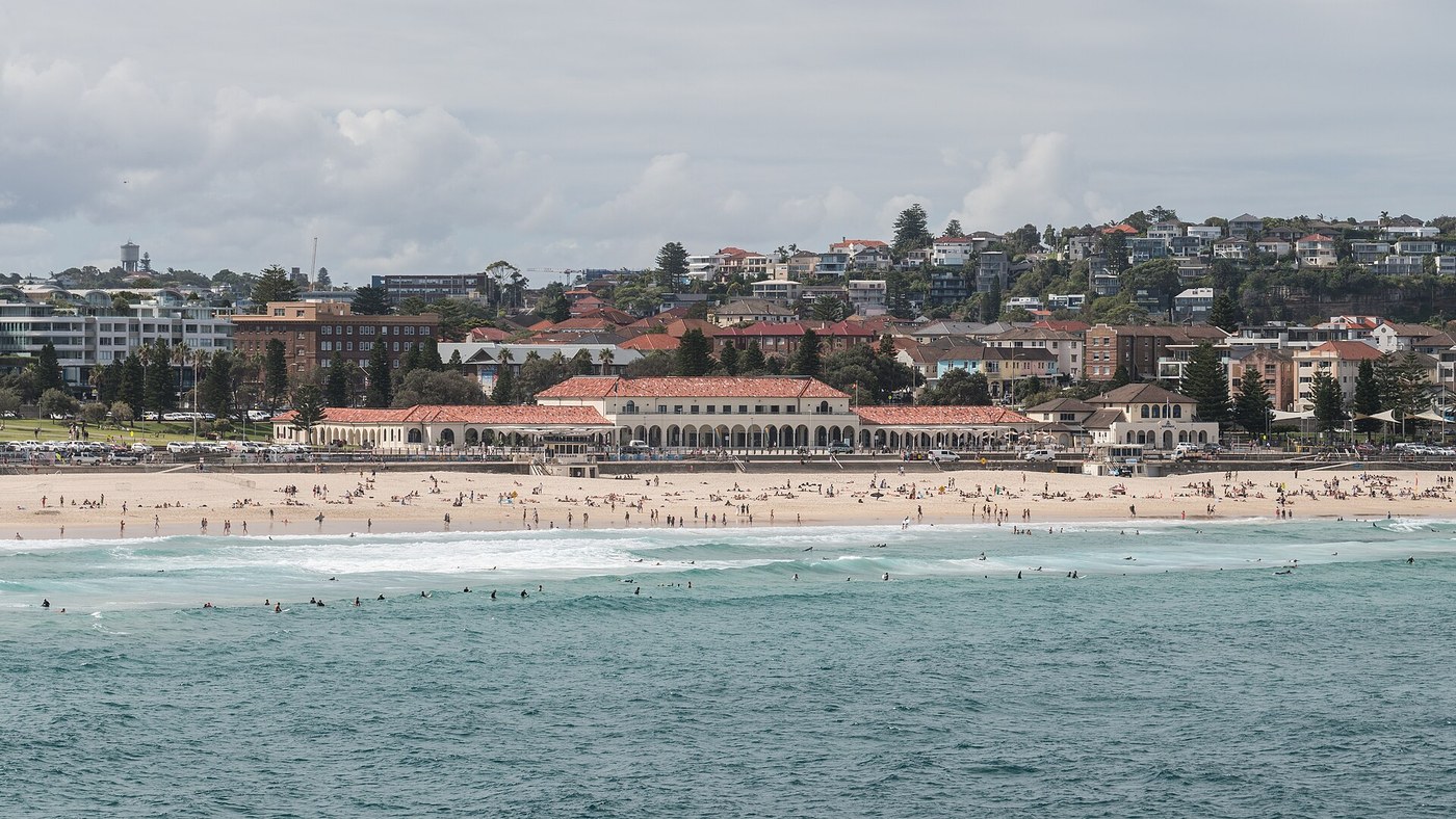 Bondi Pavilion with pale arches and a red-tiled roof behind the beach, with city buildings farther inland.
