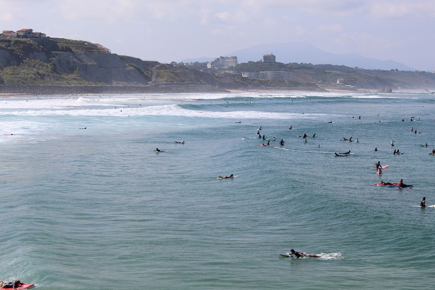 Surfers in the water off Côte des Basques in Biarritz, with the beach and coastal cliffs behind them.