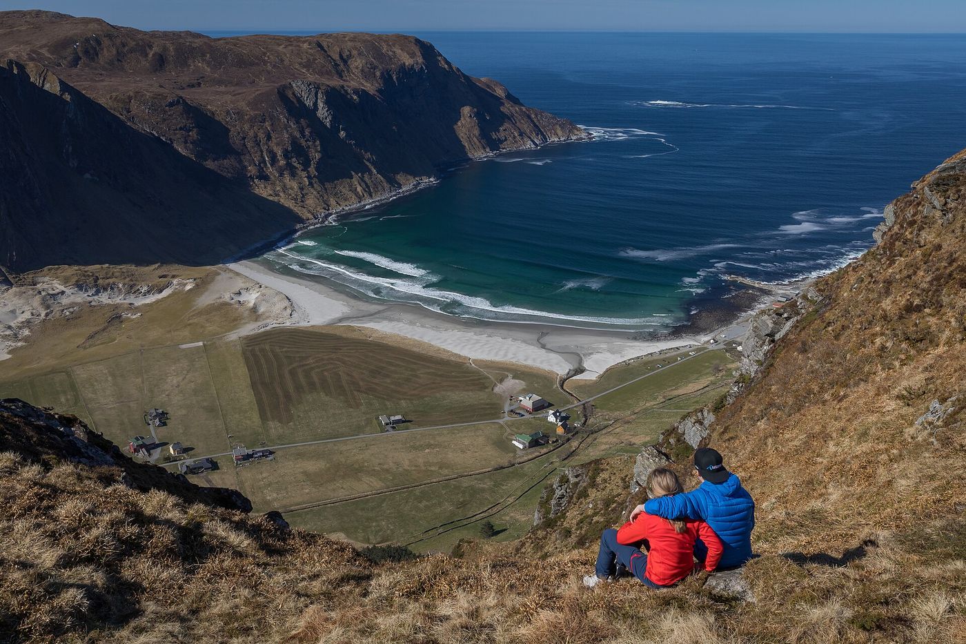 Hoddevik beach, fields and scattered houses seen from above, with two seated visitors in the foreground.