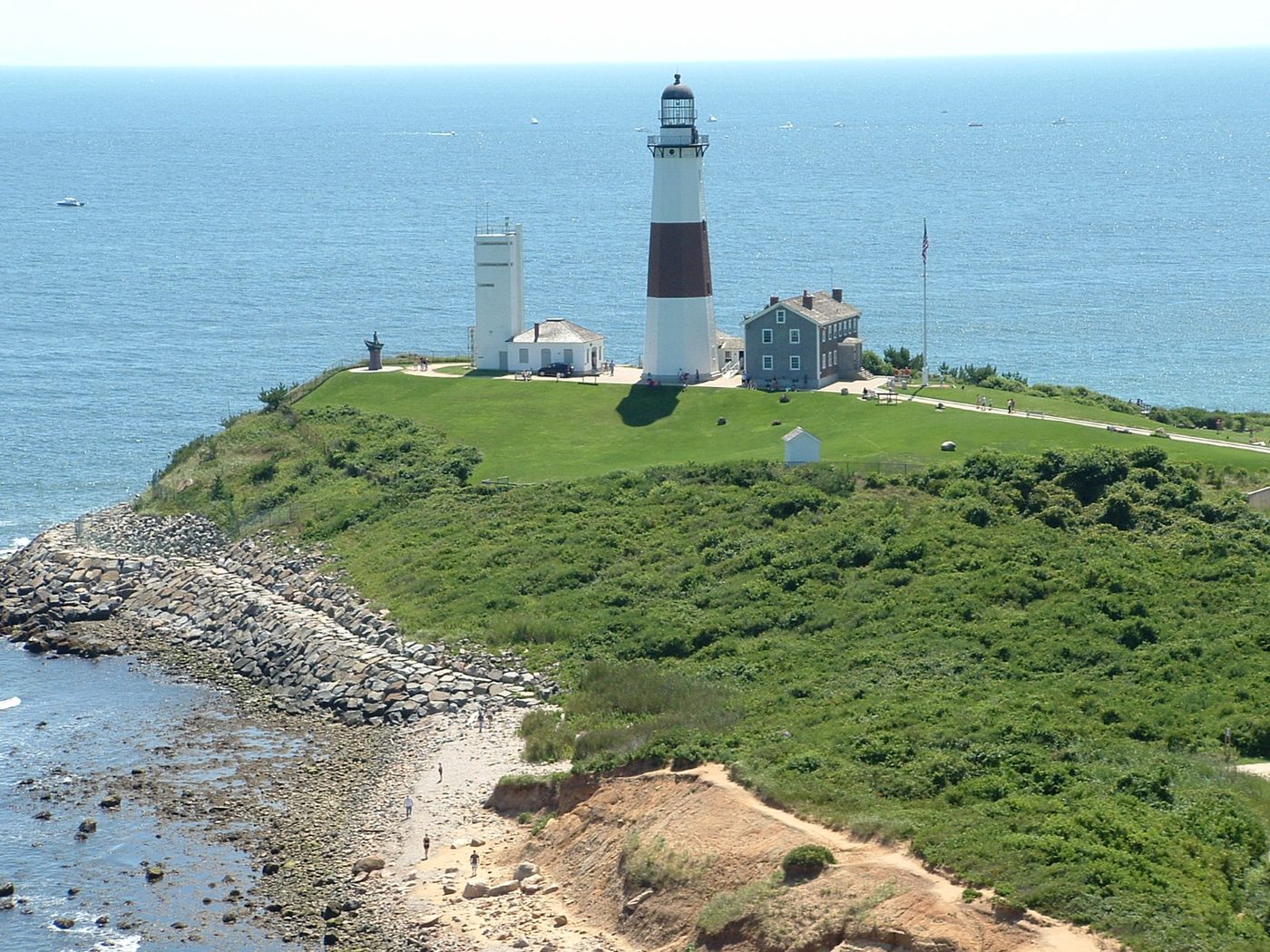 Montauk Point Lighthouse and nearby buildings on a grassy headland above a rocky shoreline.