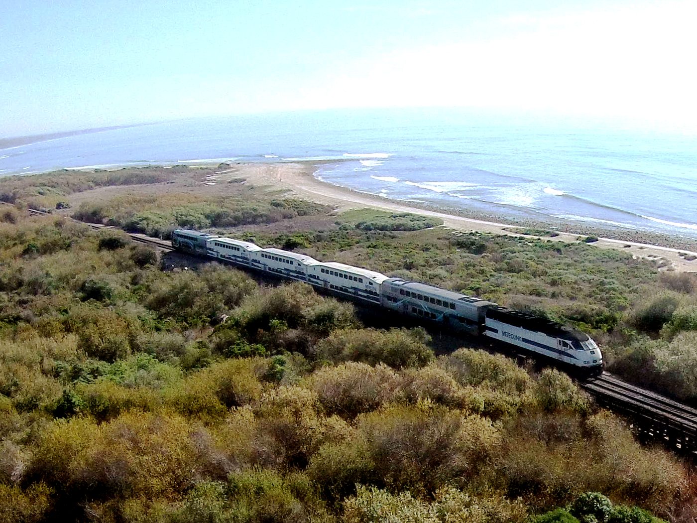 A passenger train beside the shoreline at Trestles, with coastal vegetation and waves beyond the railway.